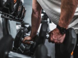 person in gray shirt holding black dumbbell